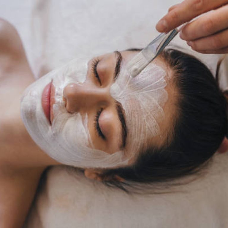 Woman getting facial nourishing mask by beautician at spa salon. Skincare spa relax concept.